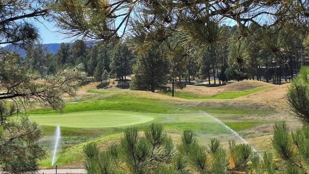 A golf course with a water fountain, surrounded by pine trees and a clear sky. - Grisham’s View Condo| Cozy w/Golf Course Views! (Ruidoso)