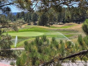 A golf course with a water fountain, surrounded by pine trees and a clear sky. - Golf Course Front Condo | Ruidoso Getaway w/ (Ruidoso)