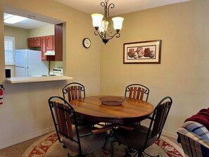 A dining room with a round table, four chairs, a chandelier, a clock, and a framed picture on the wall. - Golf Course Front Condo | Ruidoso Getaway w/ (Ruidoso)