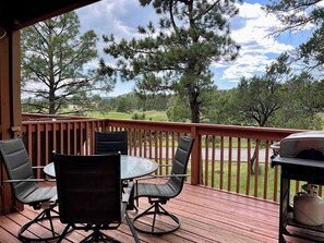 A wooden deck with outdoor furniture, a grill, and a view of a green landscape. - Golf Course Front Condo | Ruidoso Getaway w/ (Ruidoso)