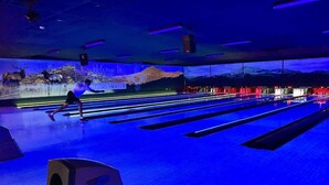 A bowling alley with multiple lanes, a person bowling, and a mural with a mountainous landscape and the text 'Welcome to Texas.' - Grisham’s View Condo| Cozy w/Golf Course Views! (Ruidoso)
