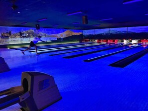 A bowling alley with multiple lanes, a person bowling, and a mural with a mountainous landscape and the text 'Welcome to Texas.'