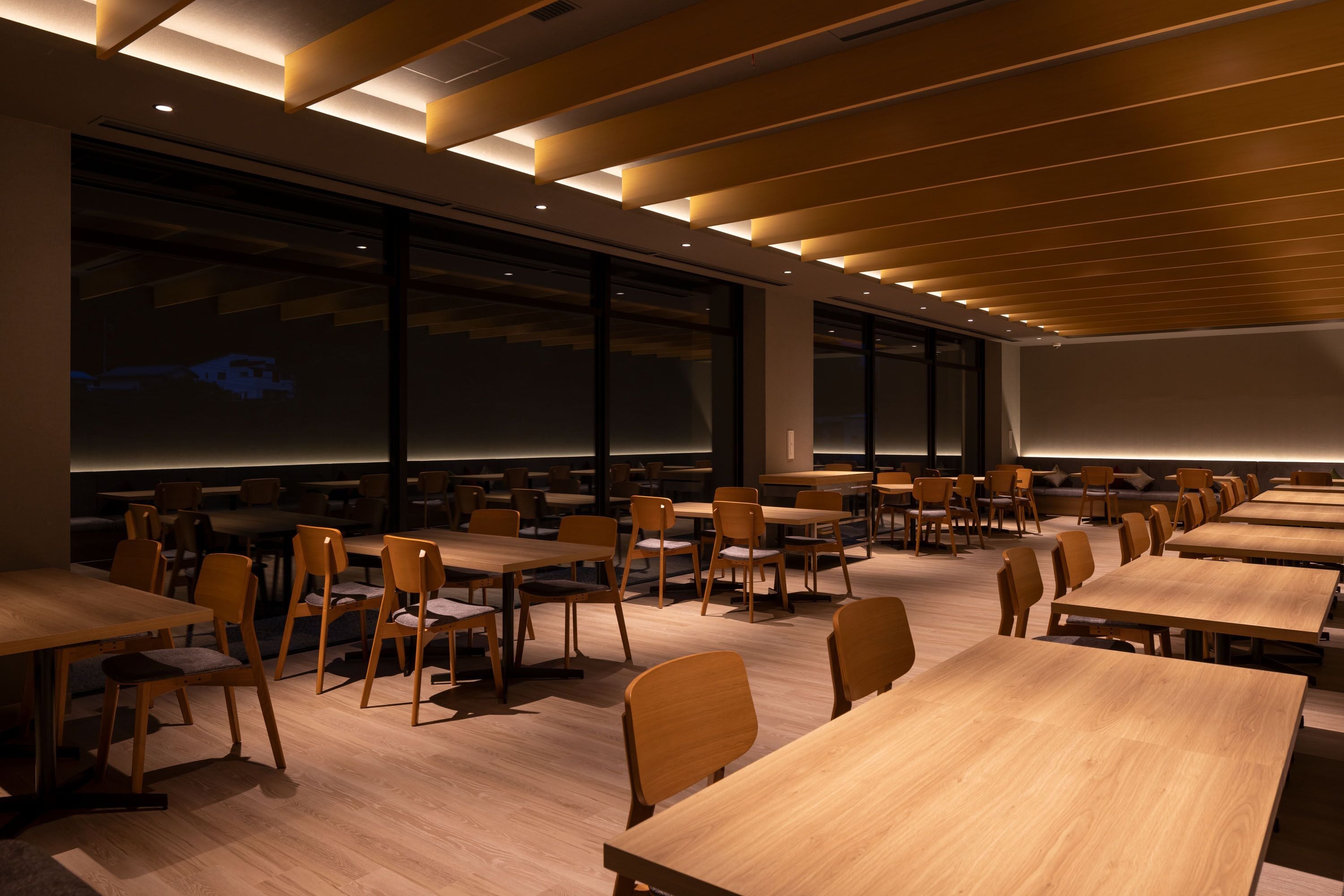 A conference room with multiple tables and chairs, large windows, and a projection screen.