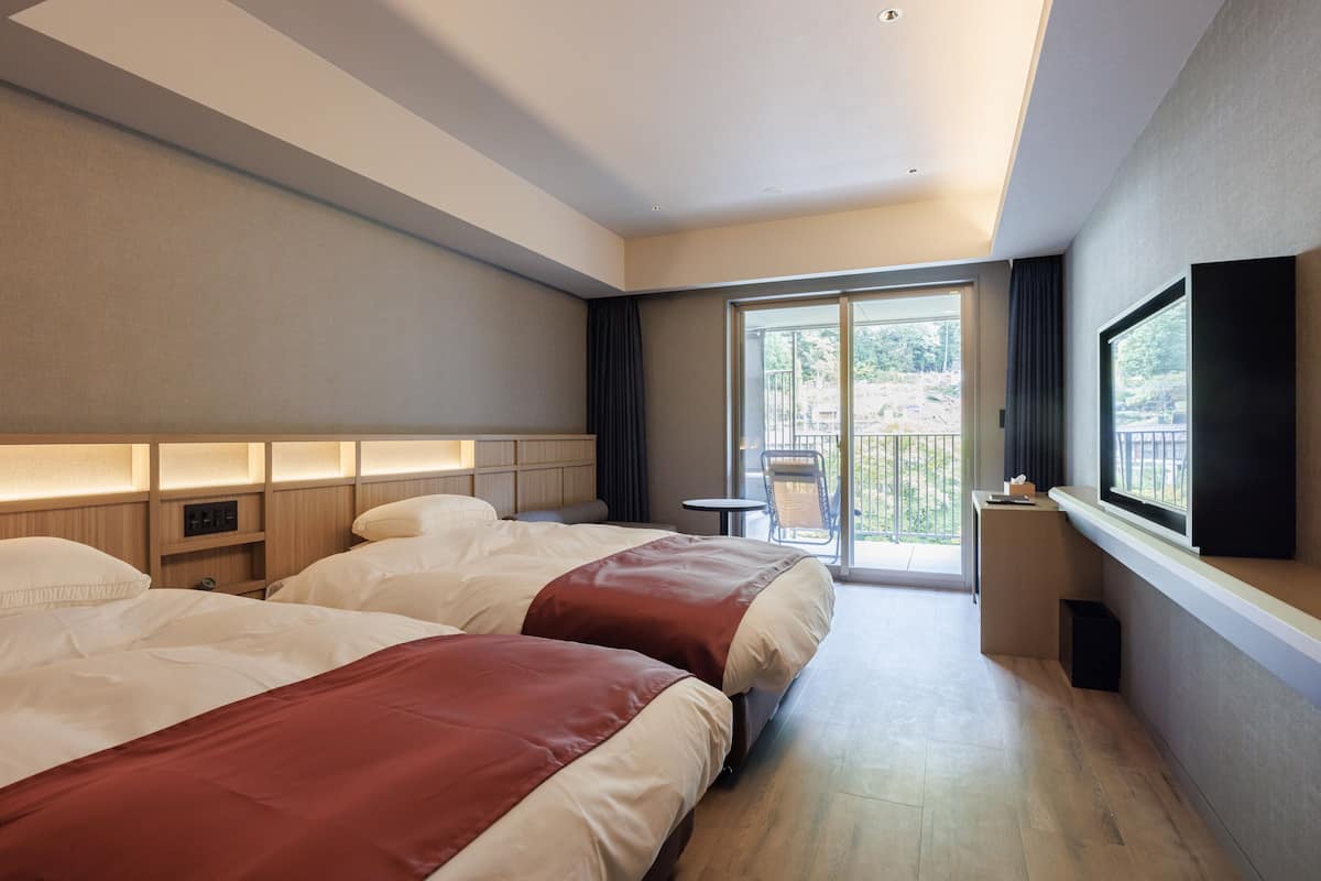 Ein Hotelzimmer mit zwei Betten, einem Balkon, einem Fernseher und einem kleinen Tisch.