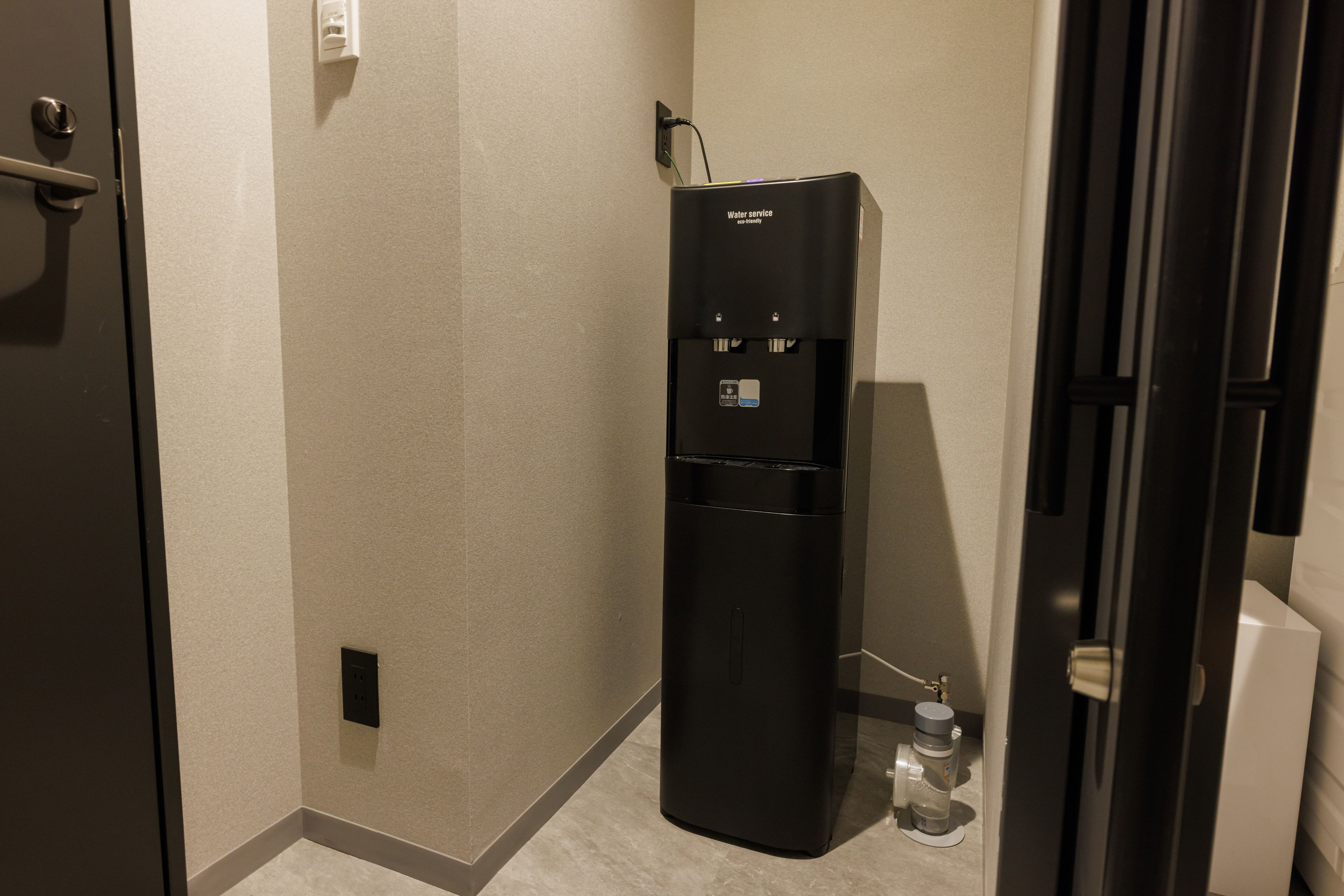 Ein kleines Hotelzimmer mit Wasserspender, Tisch und Tür.