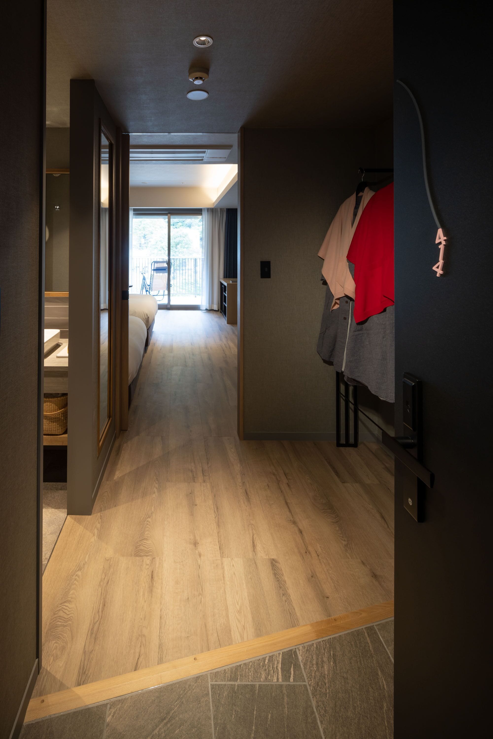 Un pasillo con suelo de madera que conduce a un dormitorio con cama y ventana.