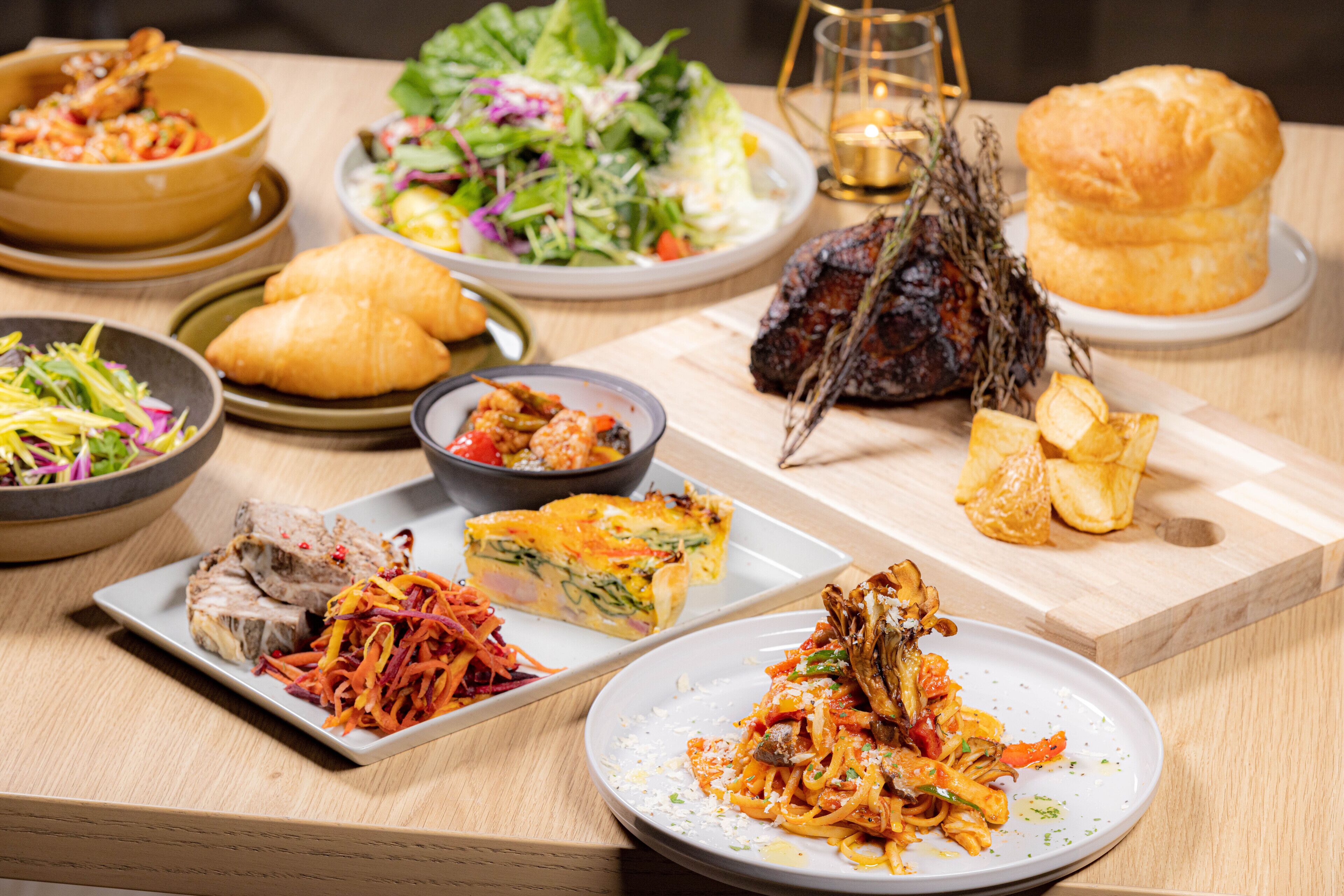 A variety of dishes including a salad, a meat dish, and a baked dish on a wooden table.