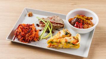 A white rectangular plate with a variety of food items including a piece of meat, a vegetable dish, and a slice of omelette.