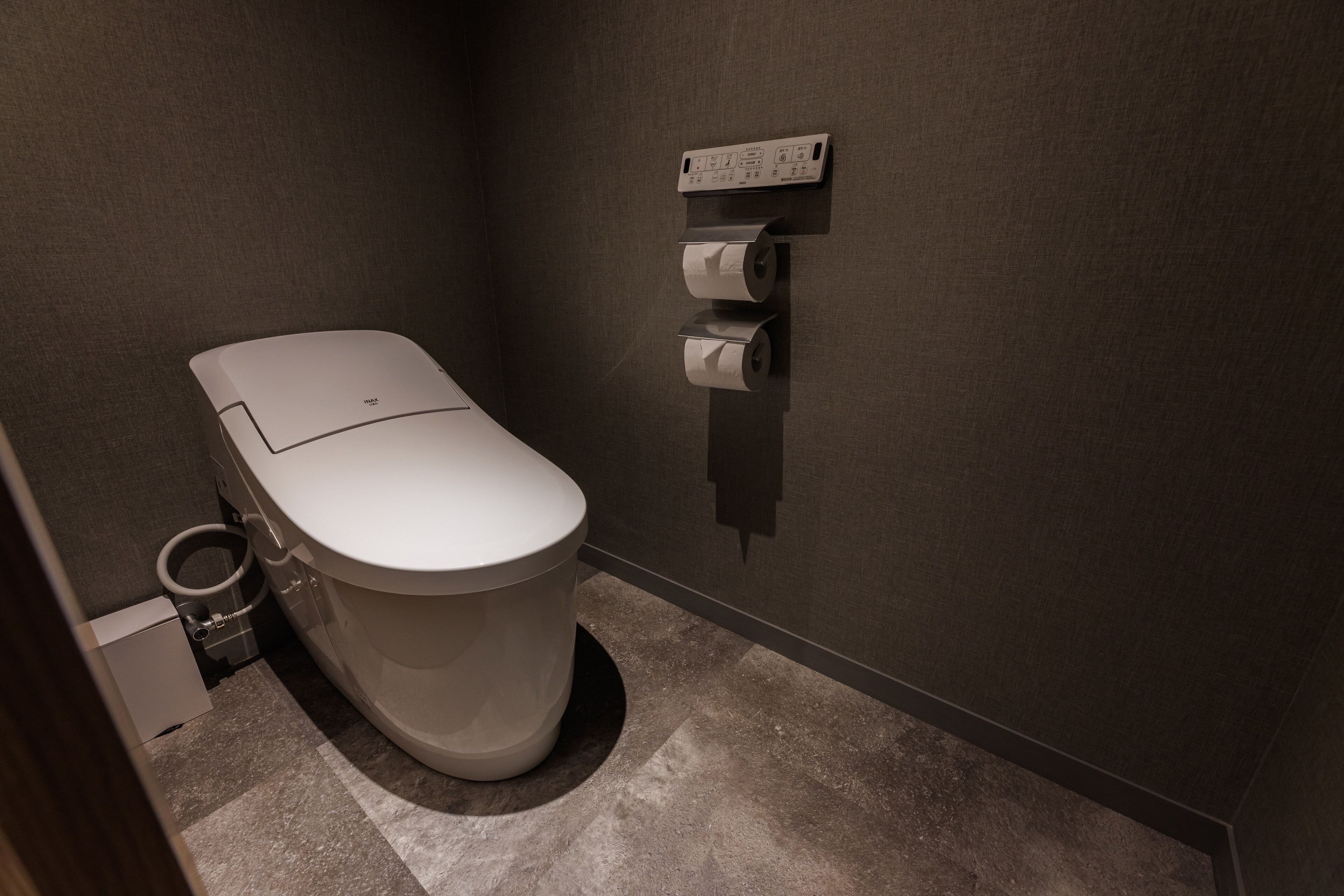 A modern bathroom with a toilet, a trash bin, and a paper towel dispenser.