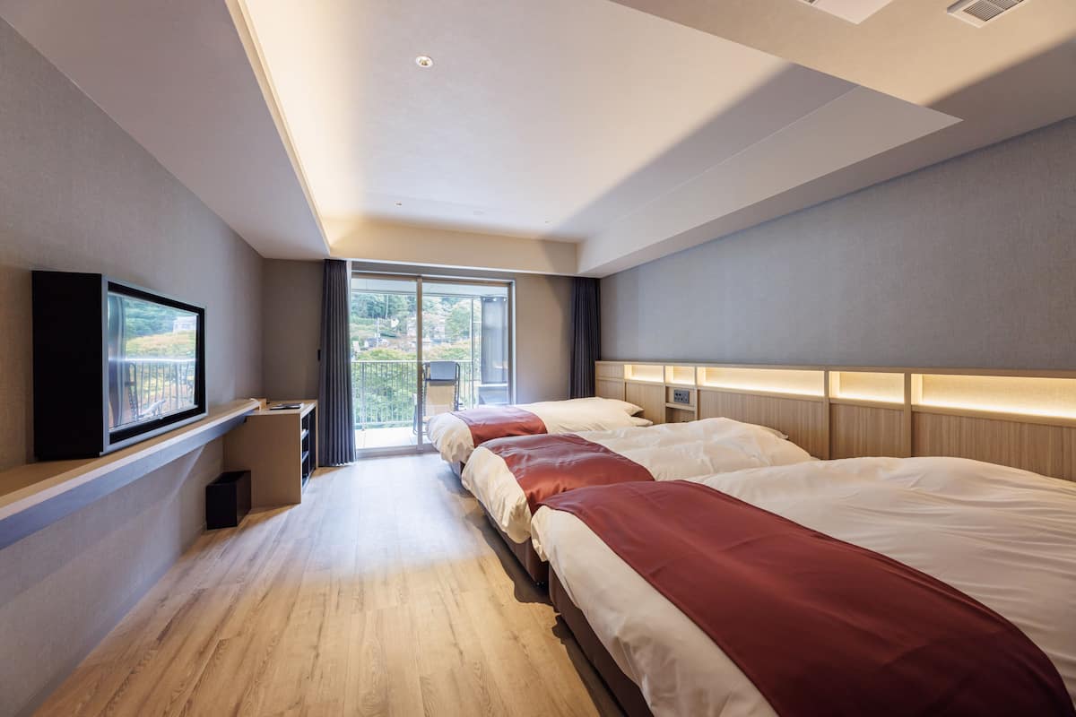 Ein Hotelzimmer mit einem großen Bett, einem an der Wand befestigten Fernseher und einem Balkon mit Stadtblick.