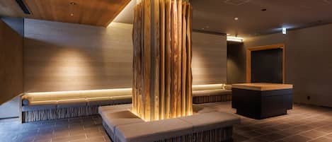 A modern lobby with a central wooden column, seating area, and a reception desk.