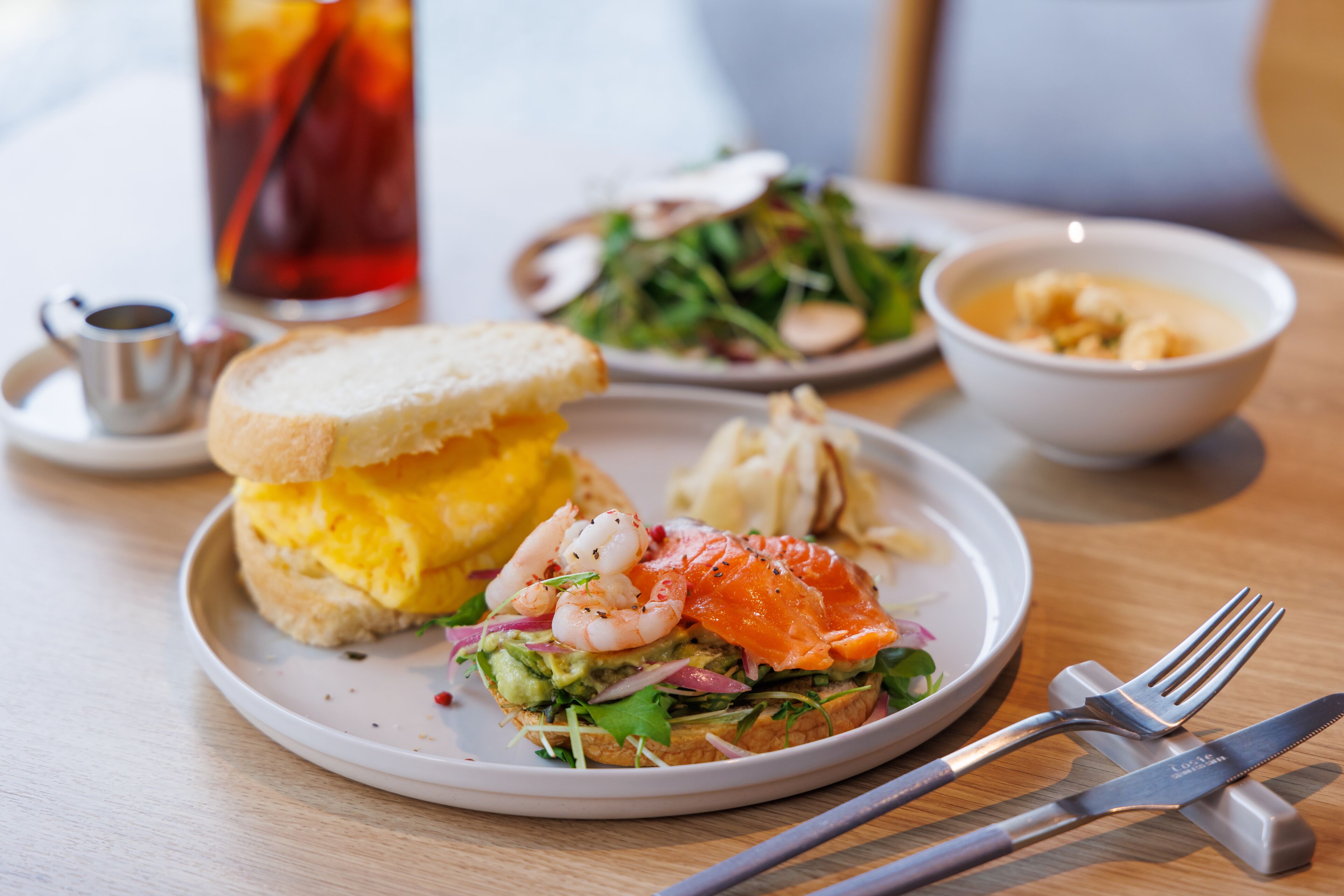 A plate with a sandwich, shrimp, and salmon on a white plate.