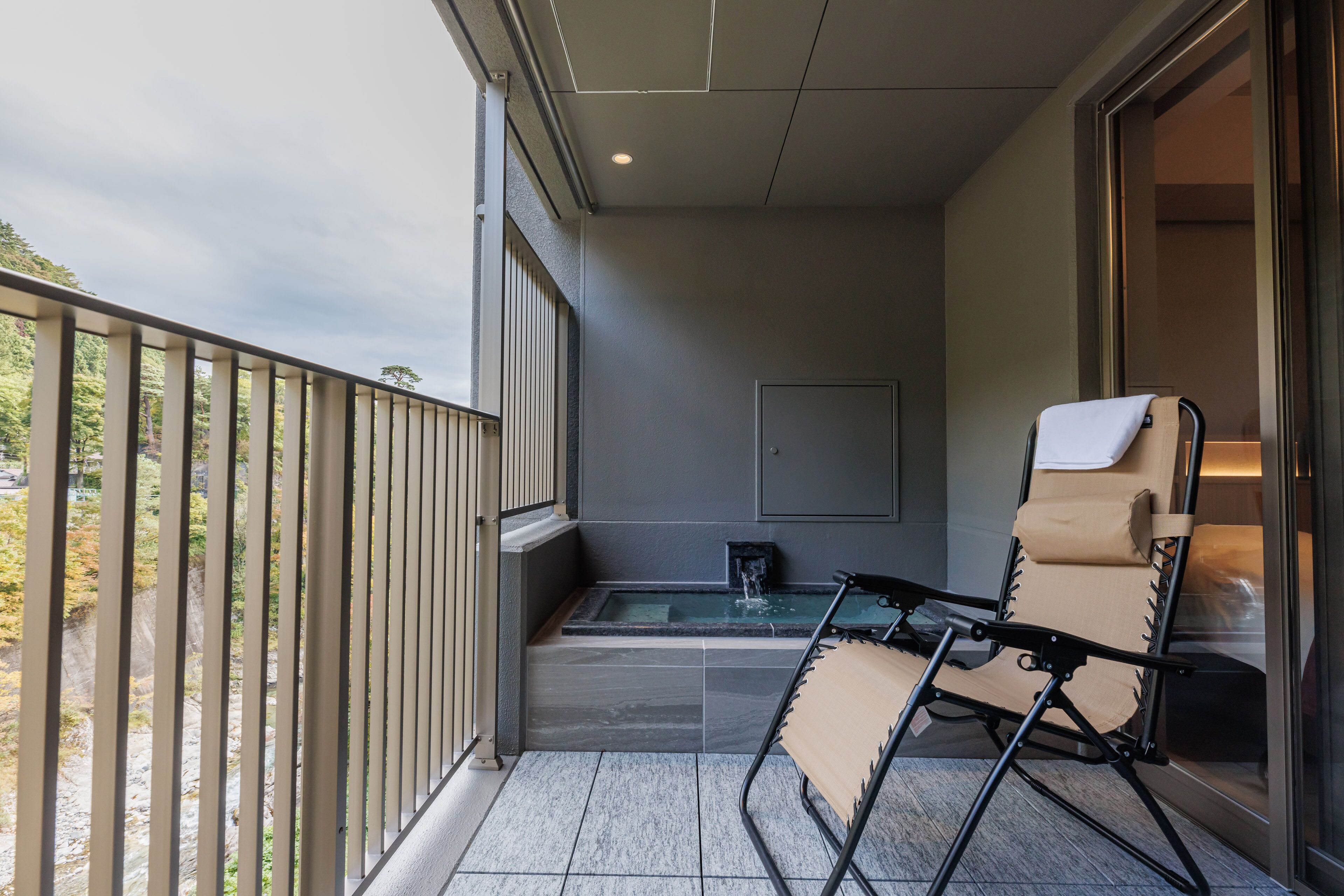 A balcony with a chair, a small table, and a view of a garden.