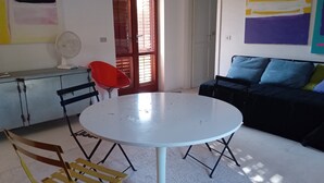 Una habitación con una mesa redonda blanca, dos sillas, un sofá y una silla roja.