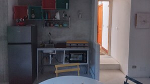Cocina compacta con refrigerador, horno y una pequeña mesa de comedor con una silla.