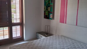 Un dormitorio con cama, cómoda, ventana con persianas y dos cuadros en la pared.