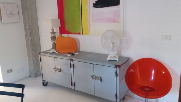 Una habitación con un armario blanco, una silla roja y una pared con arte abstracto.