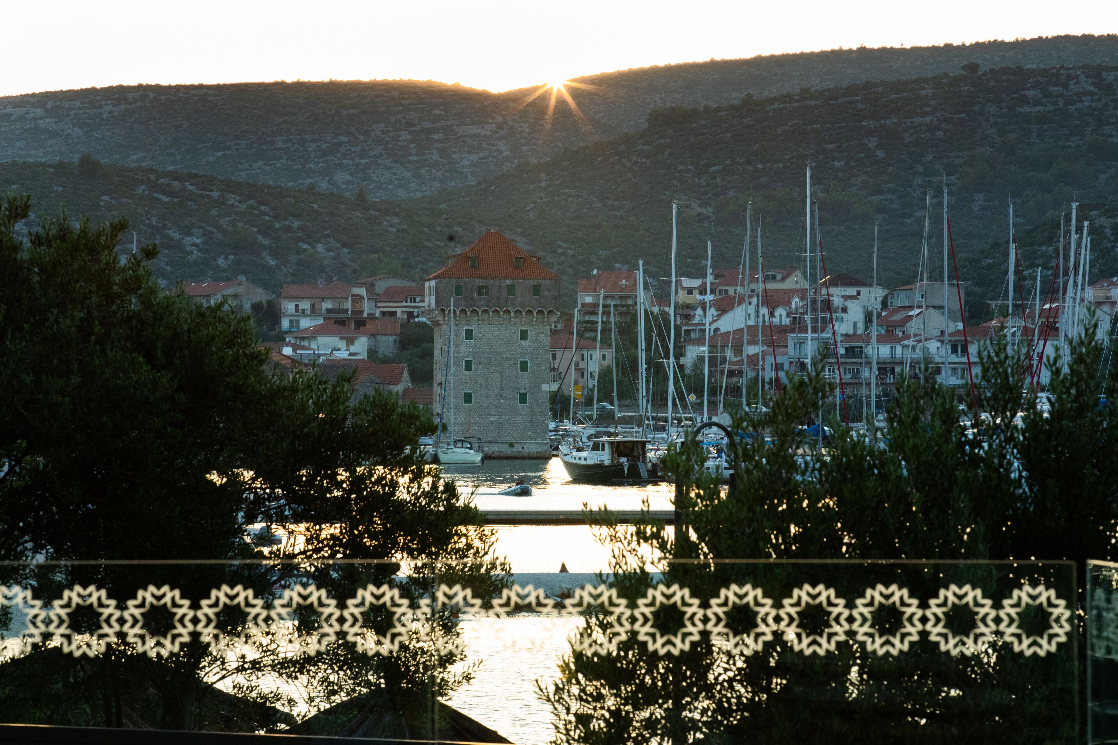 A coastal town with a prominent tower, marina with boats, and a hilly backdrop.