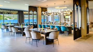 Un restaurante con varias mesas y sillas, amplias ventanas con vista al mar, e iluminación moderna.
