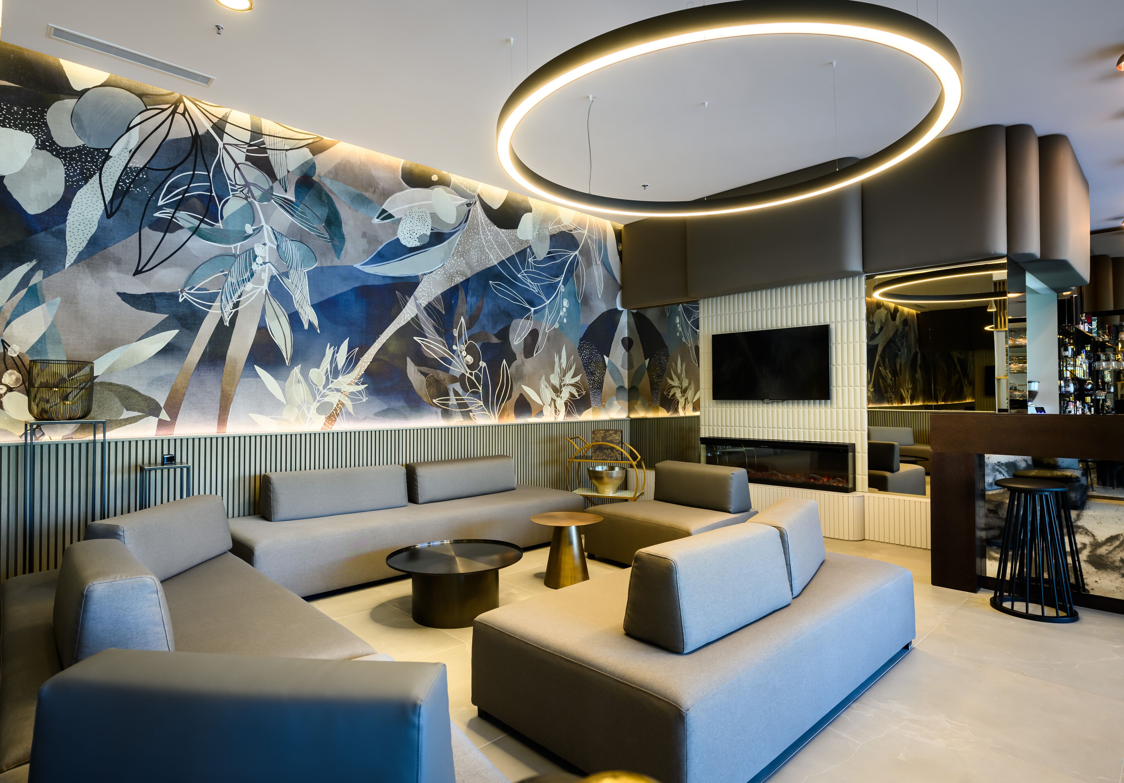A modern lounge area with a large abstract mural, comfortable seating, and a bar area with a television.