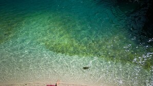 A person lying on a beach towel on a sandy beach with clear water. - Marinus Beach Hotel (Marina)