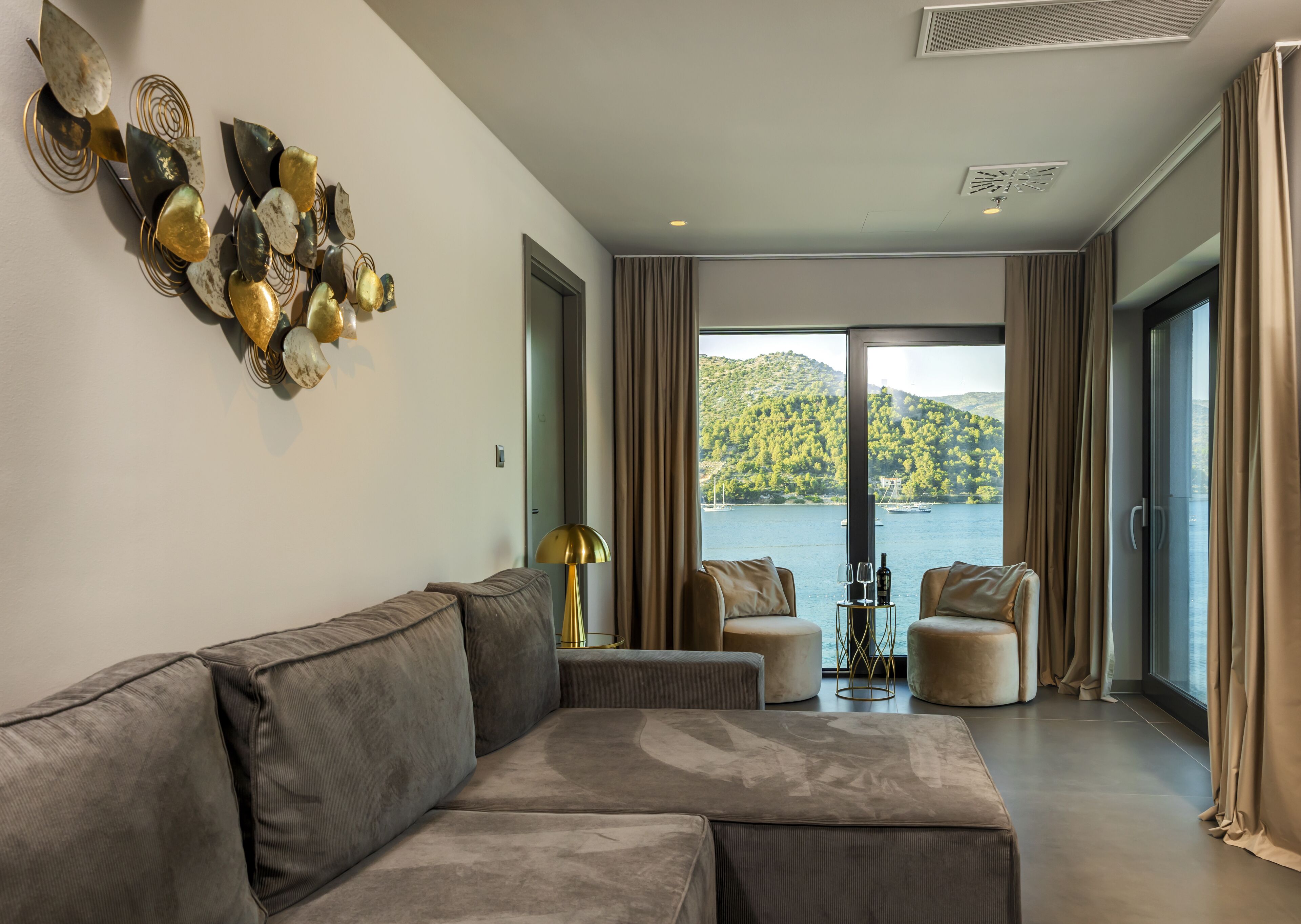 A modern living room with a grey sectional sofa, two armchairs, a gold floor lamp, and a view of a lake with boats.