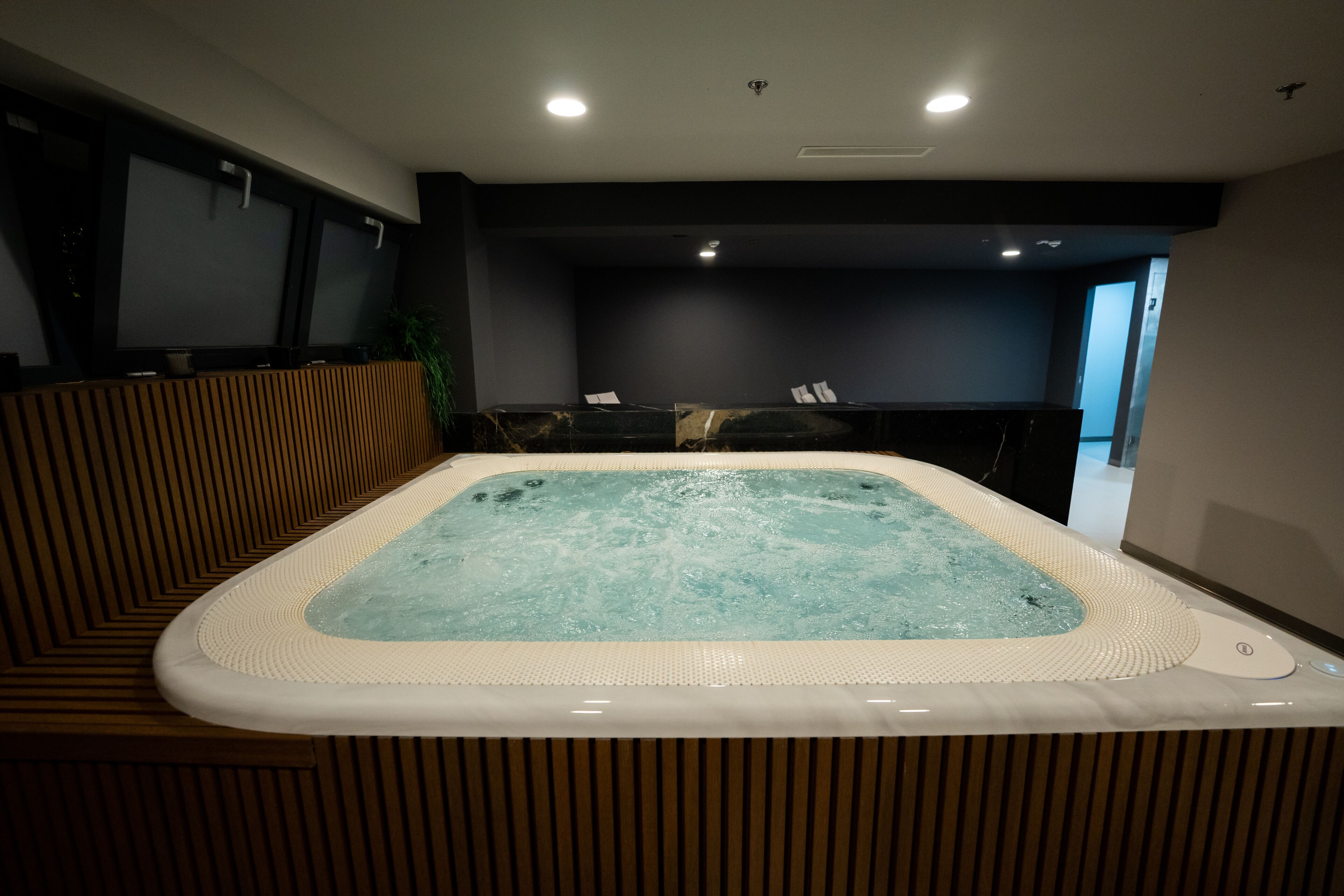 A modern spa area with a hot tub, wooden paneling, and a dark wall.