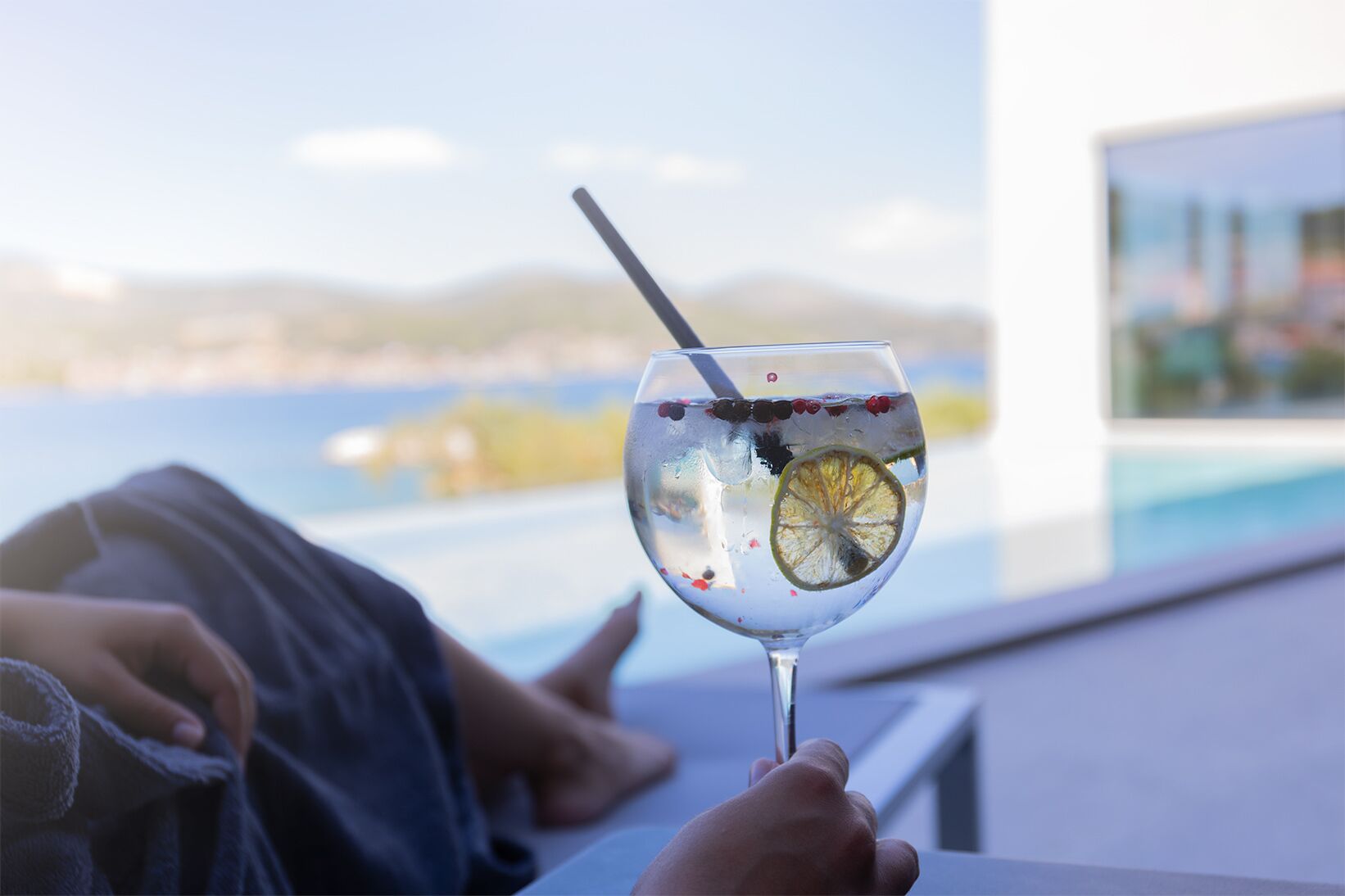 A glass of drink with a straw and a slice of lemon, held by a person.