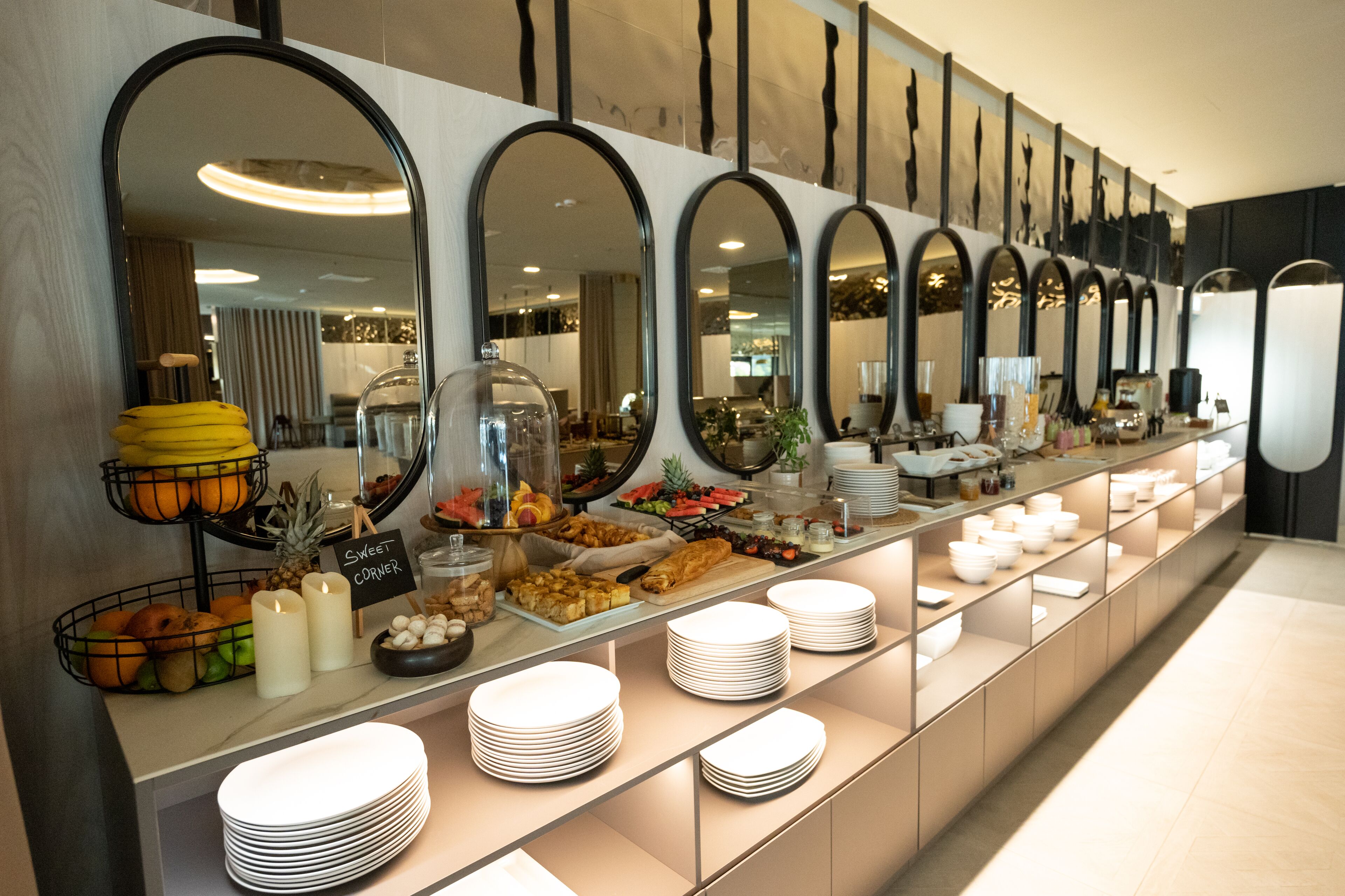 Een buffetgedeelte met meerdere spiegels, een fruitpresentatie en netjes opgestapelde borden.