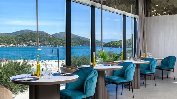 A restaurant with round tables and teal chairs, overlooking a coastal view with mountains and a clear sky. - Marinus Beach Hotel (Marina)