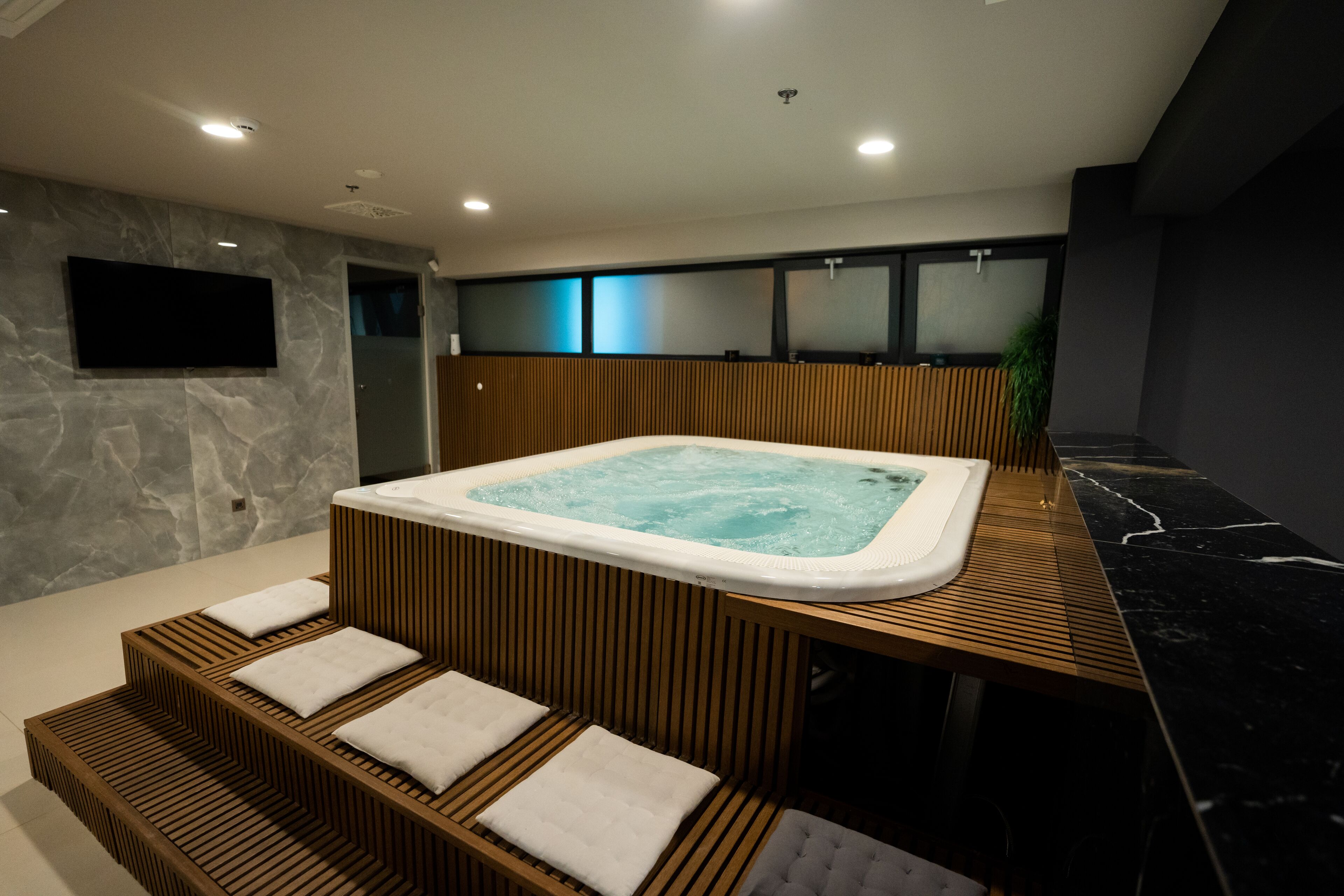 A modern spa area with a hot tub, wooden seating, and a television on the wall.