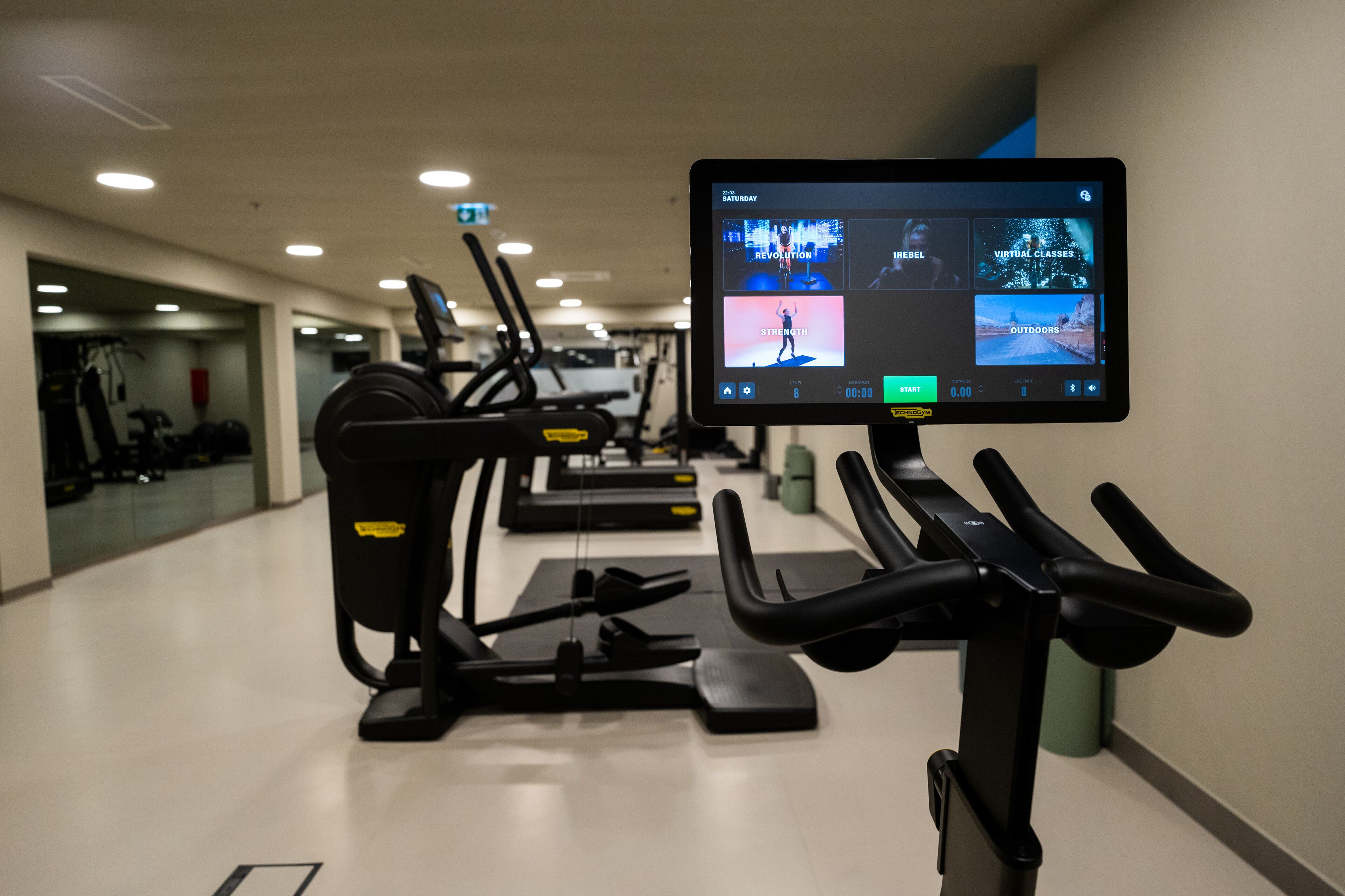 Ein Fitnessraum mit Laufbändern und einem Bildschirm, der Trainingsmöglichkeiten anzeigt.