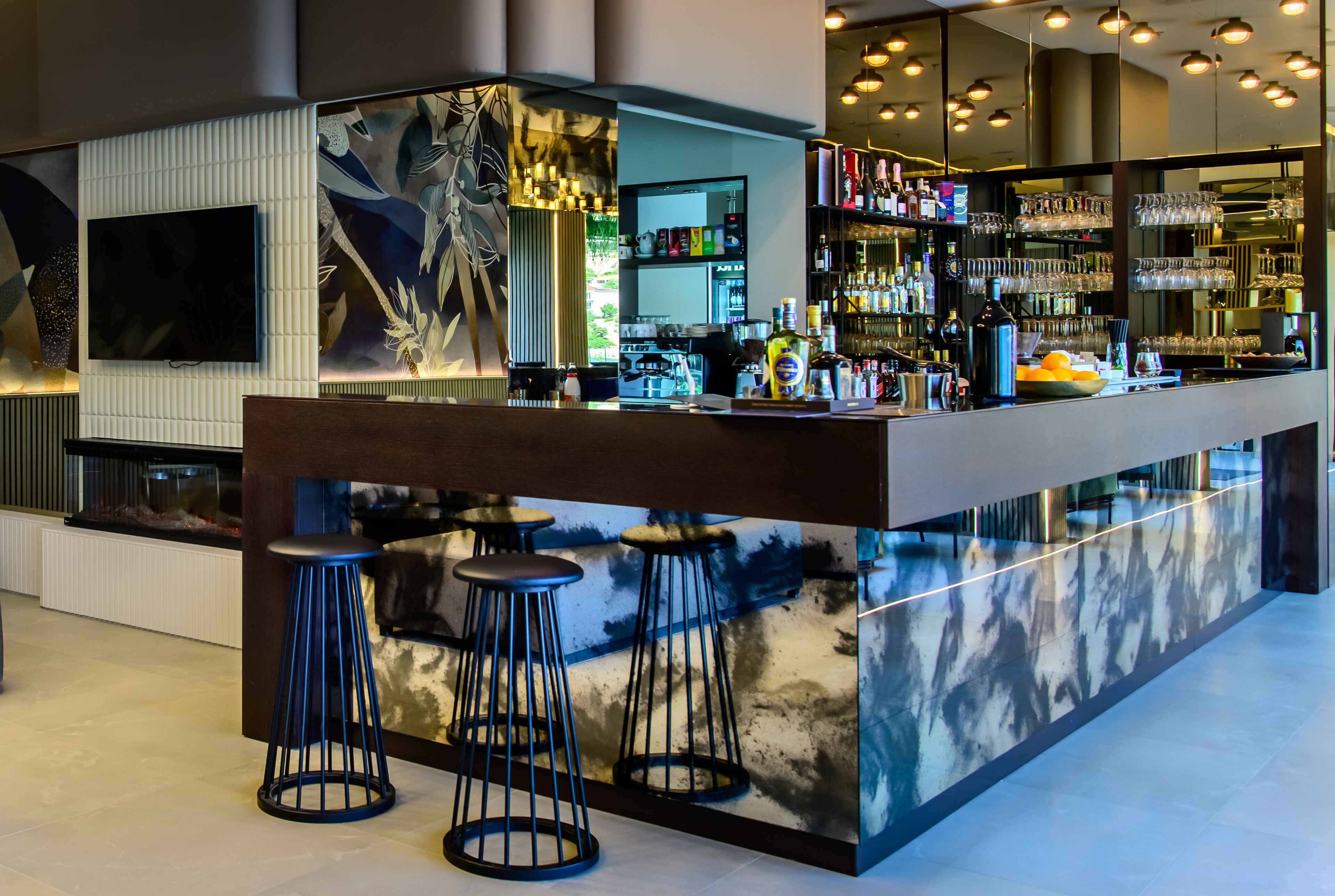 A modern bar area with a large TV screen, bar stools, and a well-stocked liquor shelf.