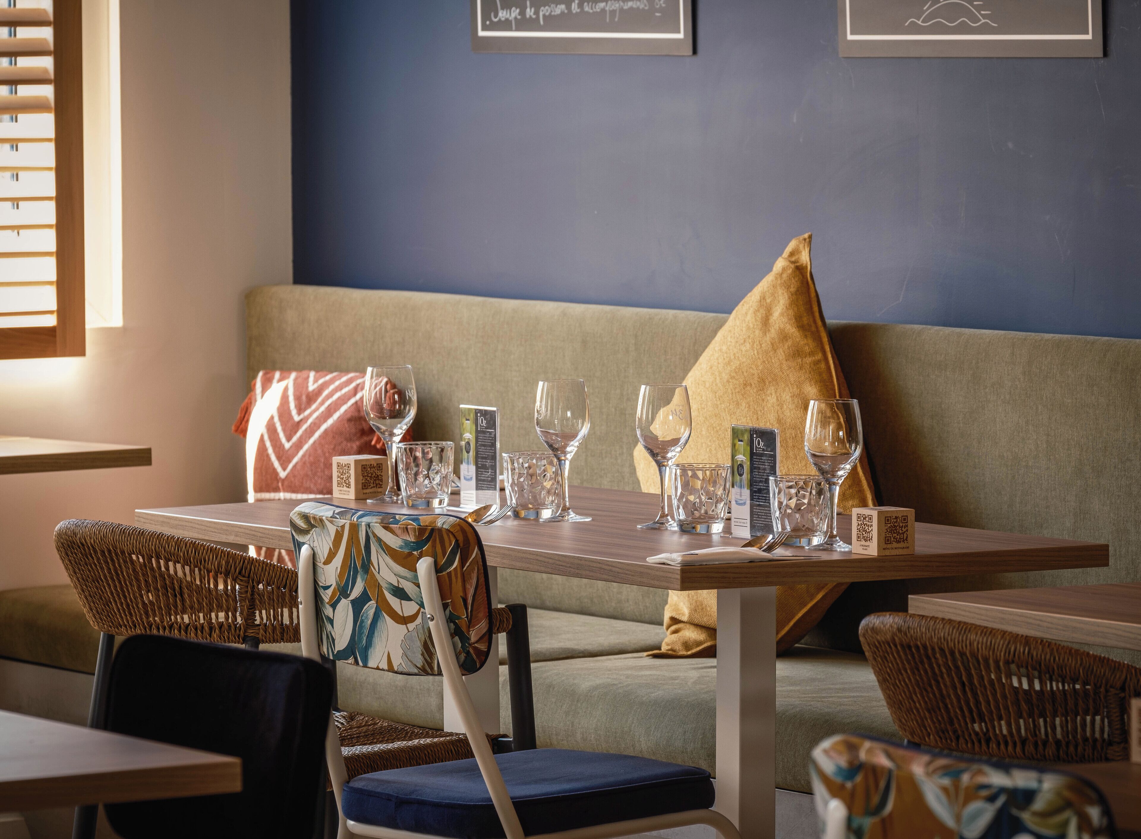 Un coin repas avec une table en bois dressée pour deux personnes, agrémenté de chaises en osier et d’un canapé.
