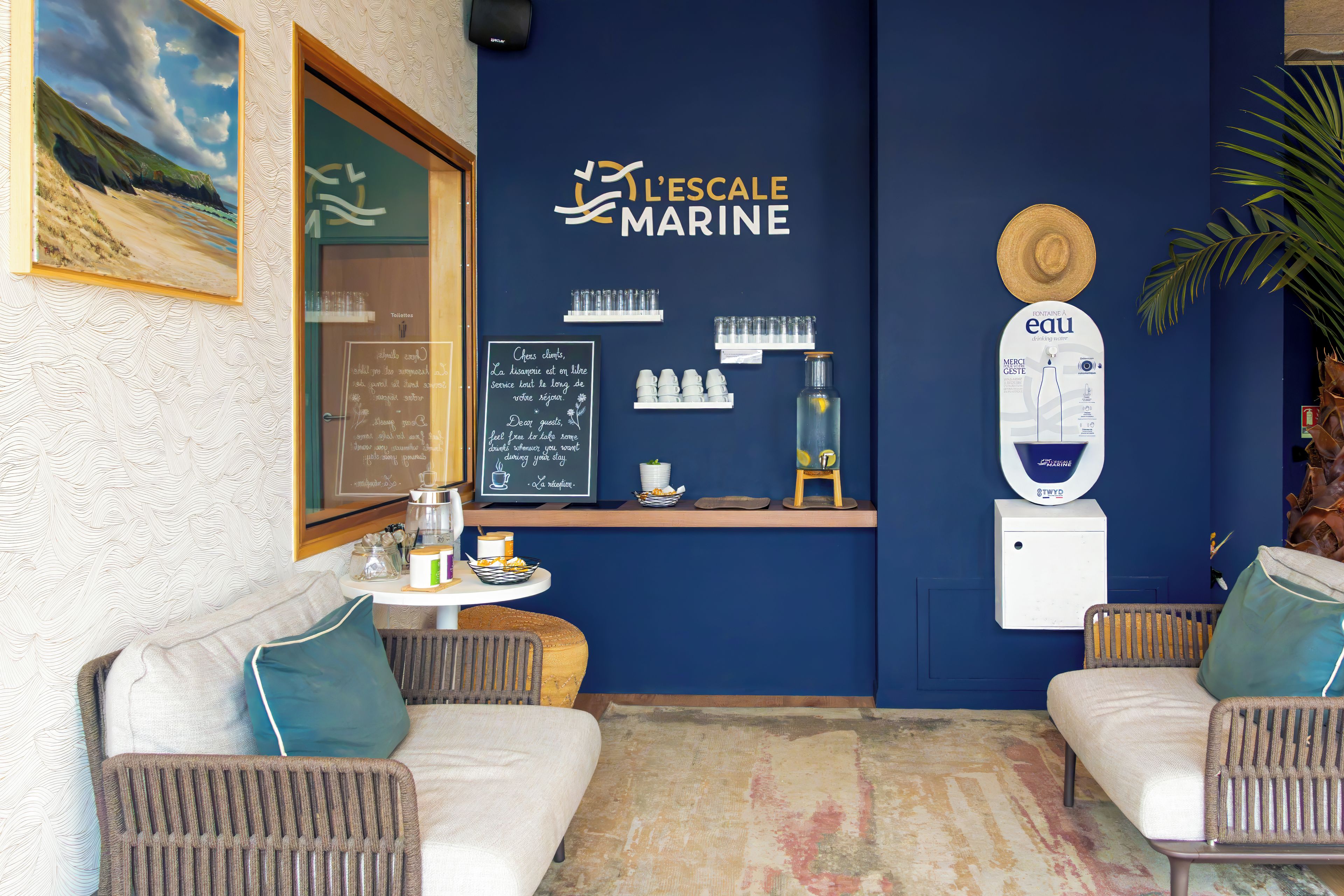 Angolo salotto con due divani, un tavolino e una parete decorata con un cartello a tema marino e servizi.
