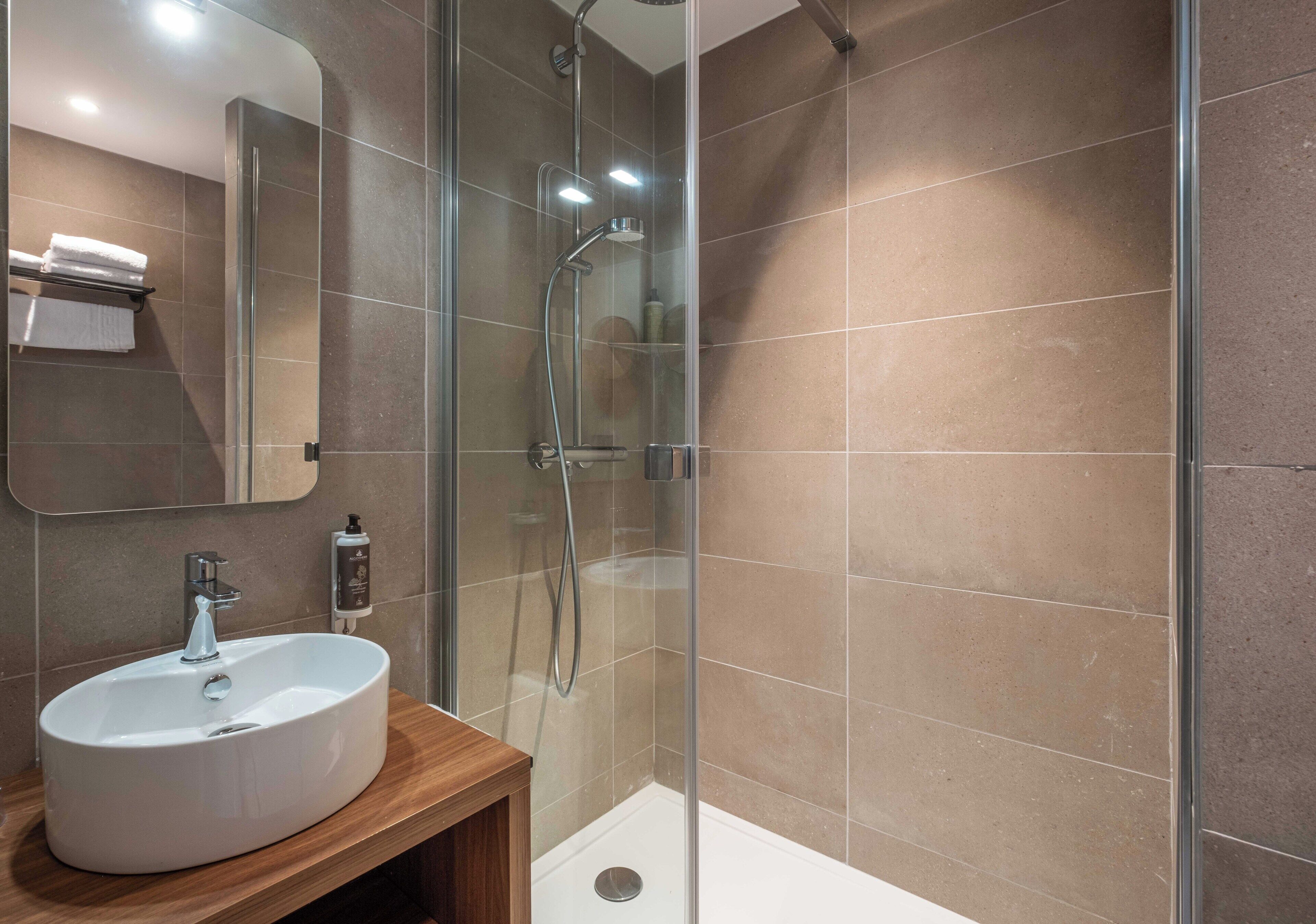 Un baño moderno con ducha de vidrio, un lavamanos blanco y un espejo.