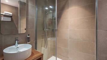 Un baño moderno con ducha de vidrio, un lavamanos blanco y un espejo.