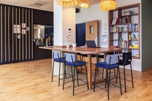 A modern workspace with a wooden table, four blue chairs, a bookshelf with books, and a decorative wall with vertical ropes.