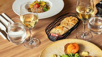 A dining table with a variety of dishes, including a salad, bread, and a plate with salmon and greens. There are also several glasses of white wine.