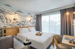 Habitación de hotel con una cama grande, una mesita de noche con una revista, un peluche de panda y un mural en la pared.
