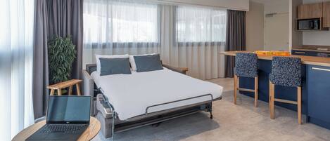 A modern hotel room with a bed, a desk, a laptop, and a small plant.