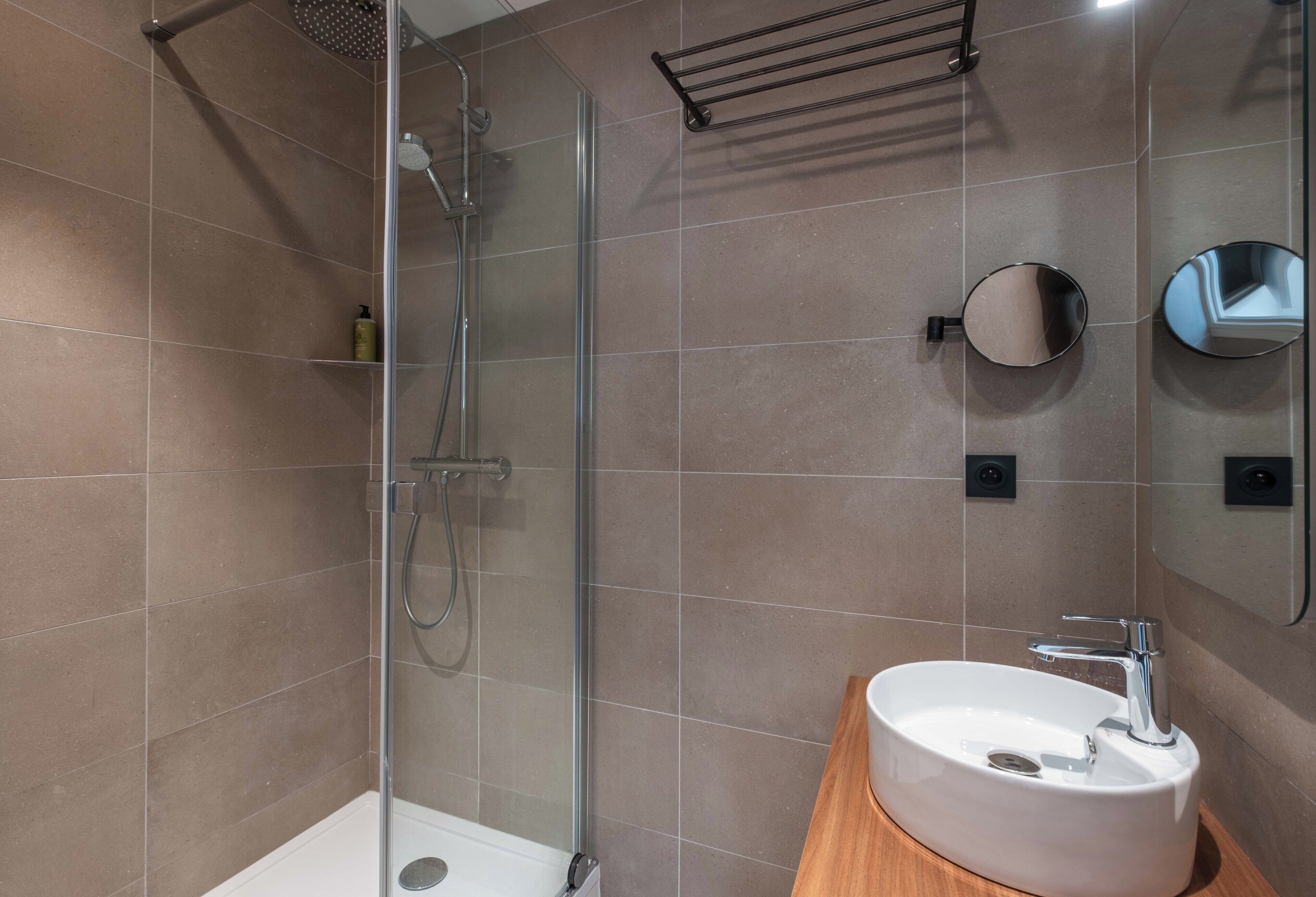 Ein modernes Badezimmer mit einer Duschkabine aus Glas, einem weißen Waschbecken und einem Spiegel.
