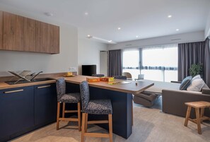 A modern kitchen with a central island, bar stools, a dining area, and a view of the city. - Hôtel l'escale marine (Crozon)