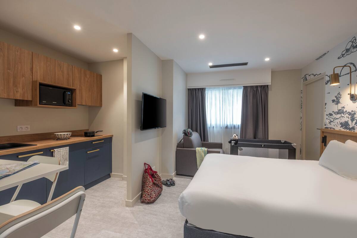 Ein Hotelzimmer mit Bett, Schreibtisch mit Stuhl, Fernseher, Mikrowelle und einer kleinen Küchenzeile.