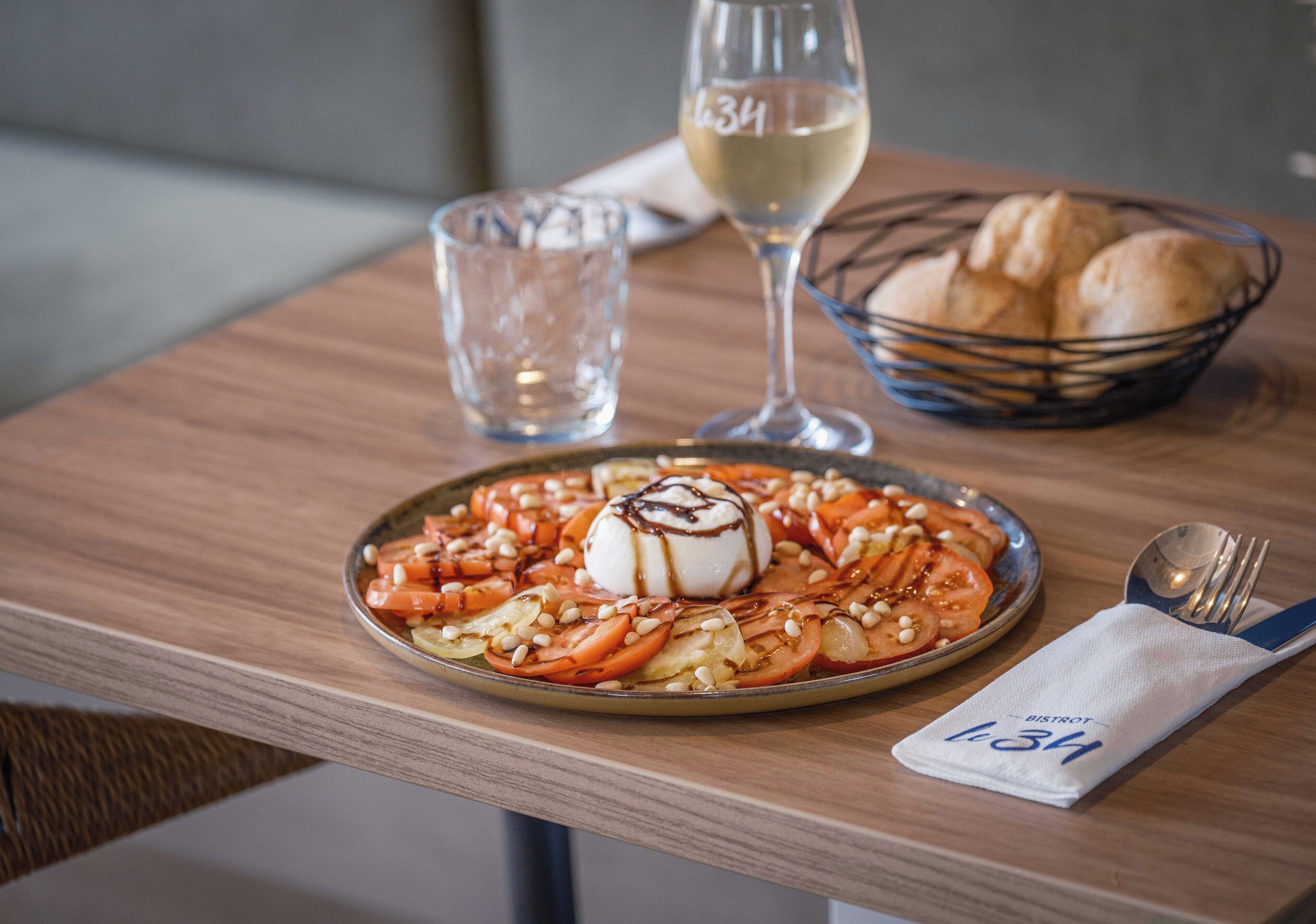 Una mesa de comedor con un plato de comida, una copa de vino blanco y una cesta de pan.