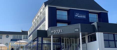 Un hotel moderno con un cartel grande que dice 'HOTEL', una escalera que lleva a la entrada y un balcón con barandilla.