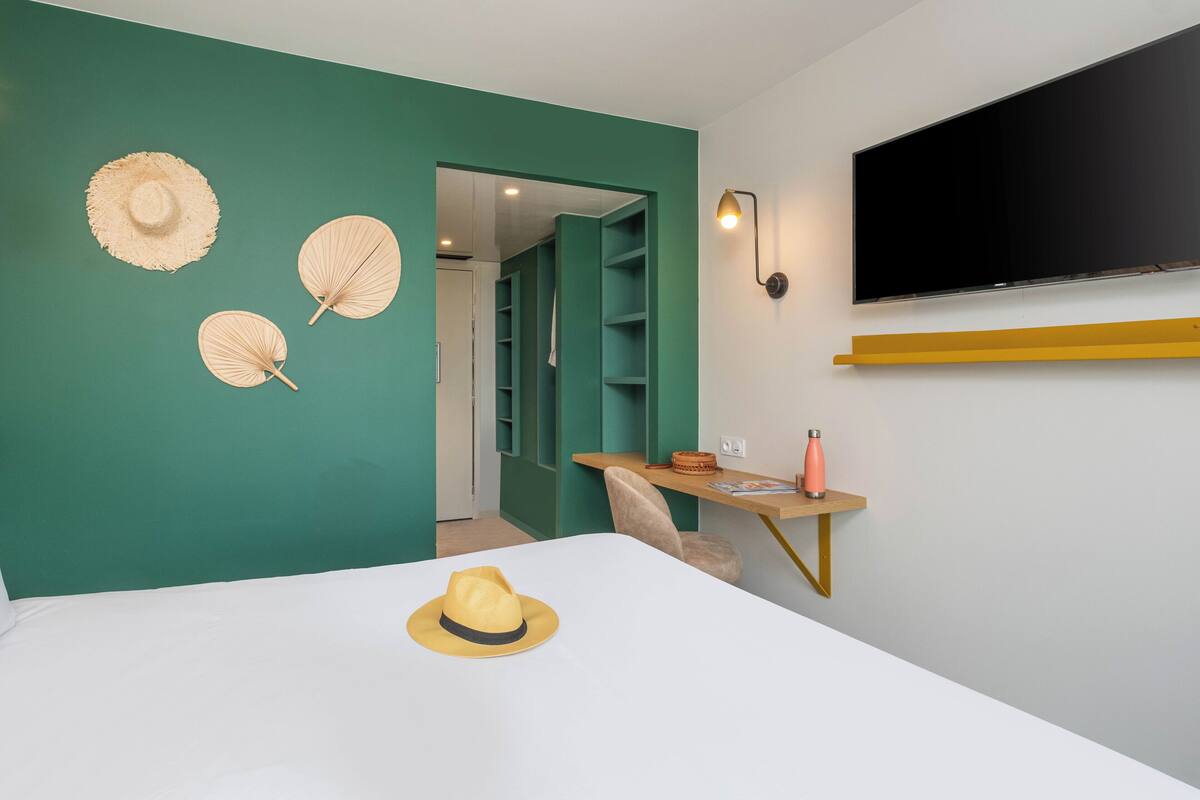 Ein Schlafzimmer mit einem Bett, einem Schreibtisch mit Lampe und einem an der Wand befestigten Fernseher.