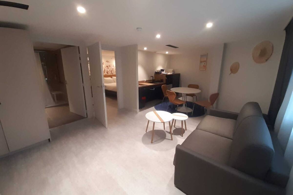 Ein modernes Wohnzimmer mit einer Couch, einem Esstisch mit Stühlen und einem durch eine offene Tür einsehbarer Küchenbereich.