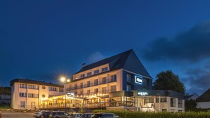 A multi-story hotel with a prominent 'HOTEL' sign, outdoor seating area, and a parking lot. - Hôtel l'escale marine (Crozon)