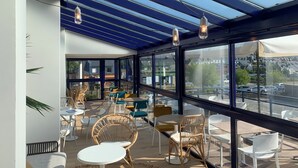 A modern café with glass walls, wicker furniture, and hanging light fixtures. - Hôtel l'escale marine (Crozon)